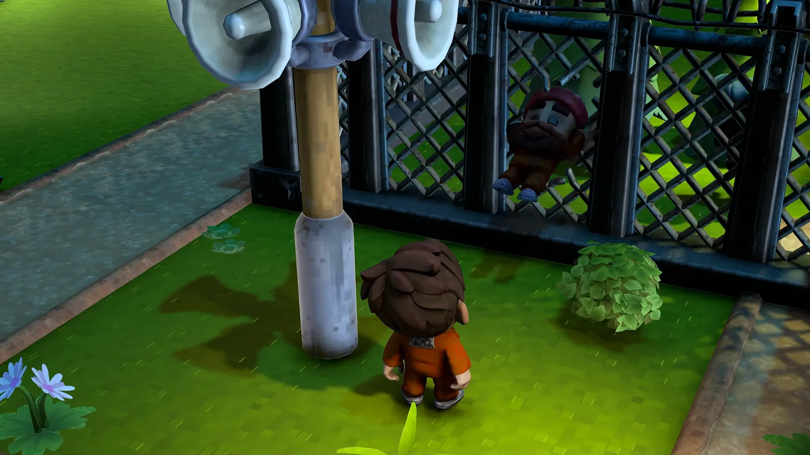 An inmate in an orange jumpsuit climbing a chain-link perimeter fence directly beneath a pair of loudspeaker horns while a crewmate walks the grass below in The Escapists 3