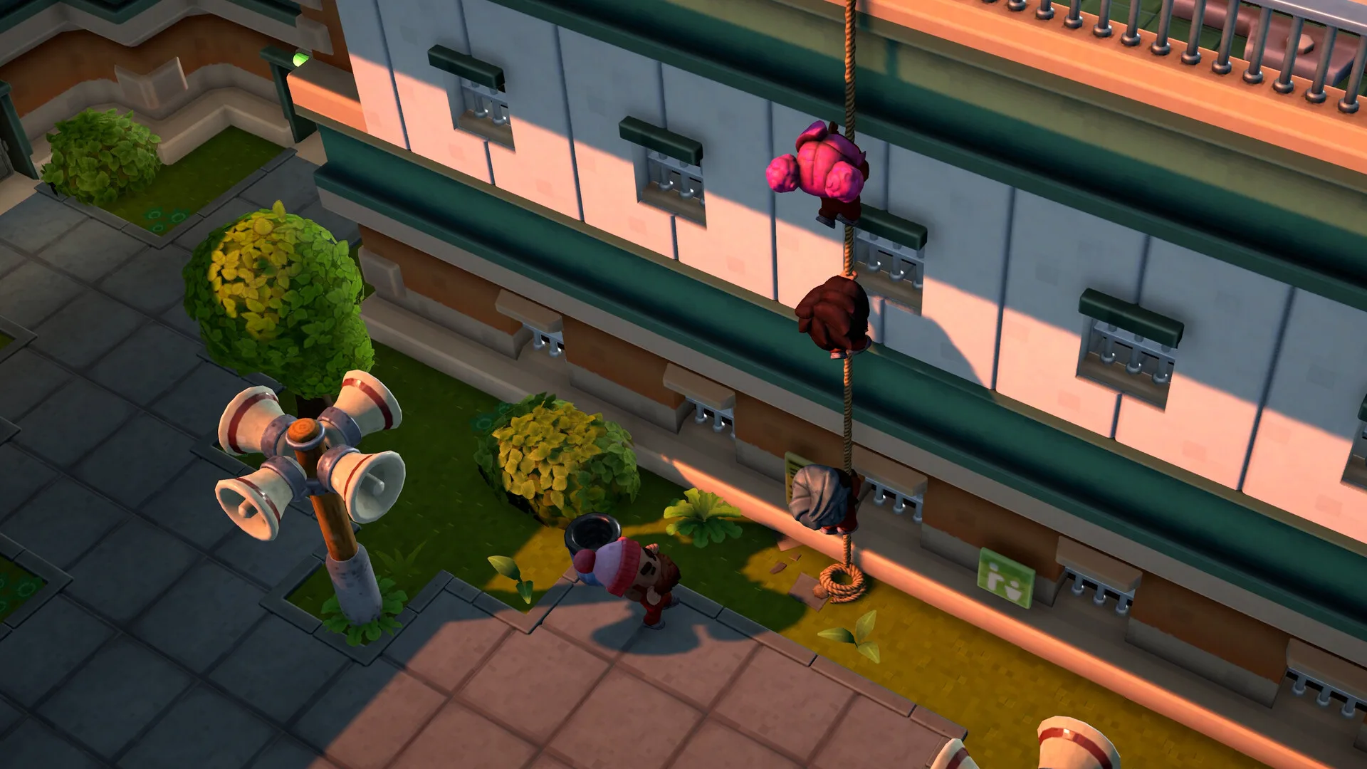 Official The Escapists 3 screenshot showing an outdoor prison yard with a cream-colored cell-block building with barred windows and green trim in the 3D isometric view